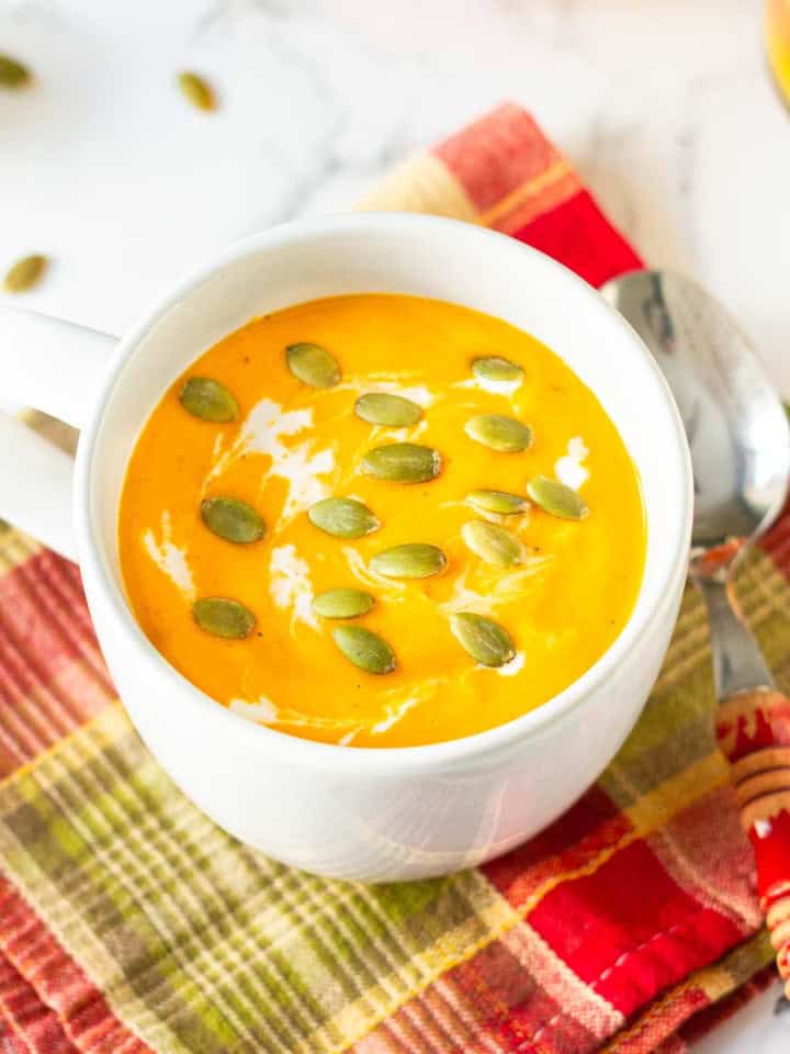 roasted pumpkin soup in a white soup mug with a spoon on a red check napkin.