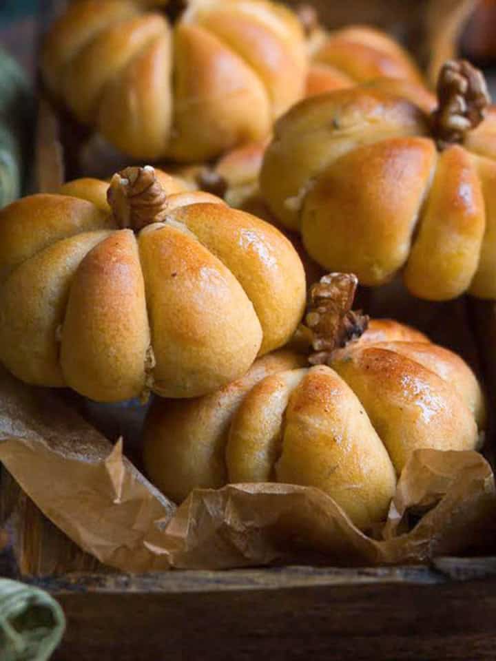 pumpkin bread rolls piled up in a wooden tray.