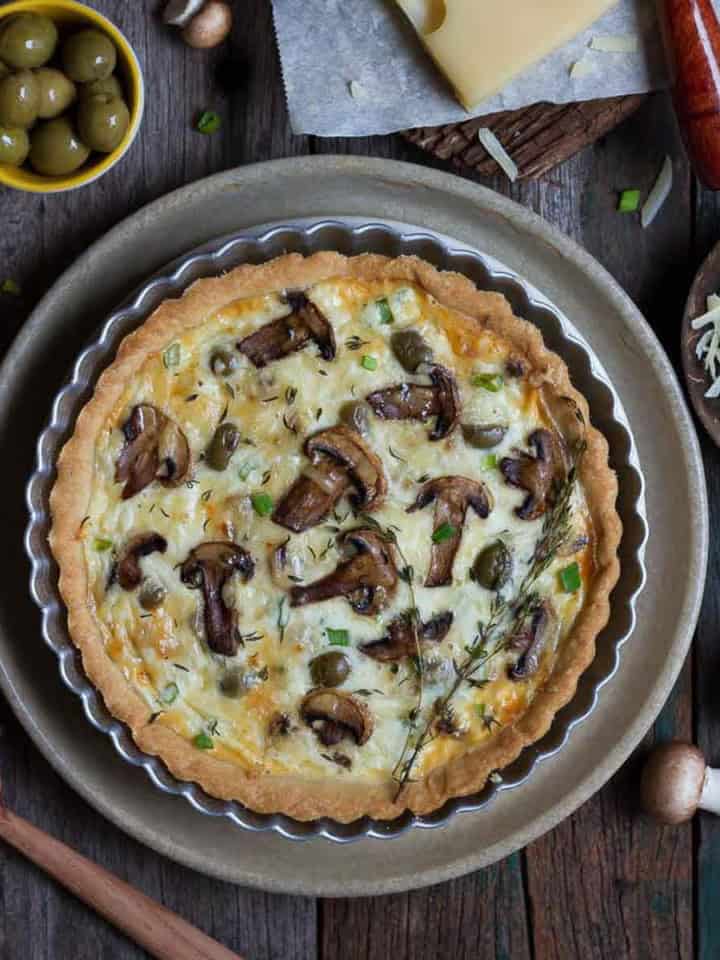 mushroom quiche on a platter with ingredients in the background.