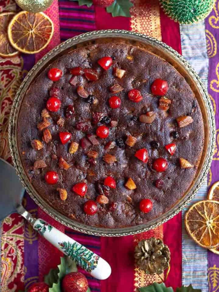 christmas rum cake on a serving platter on a colorful runner with a cake server.